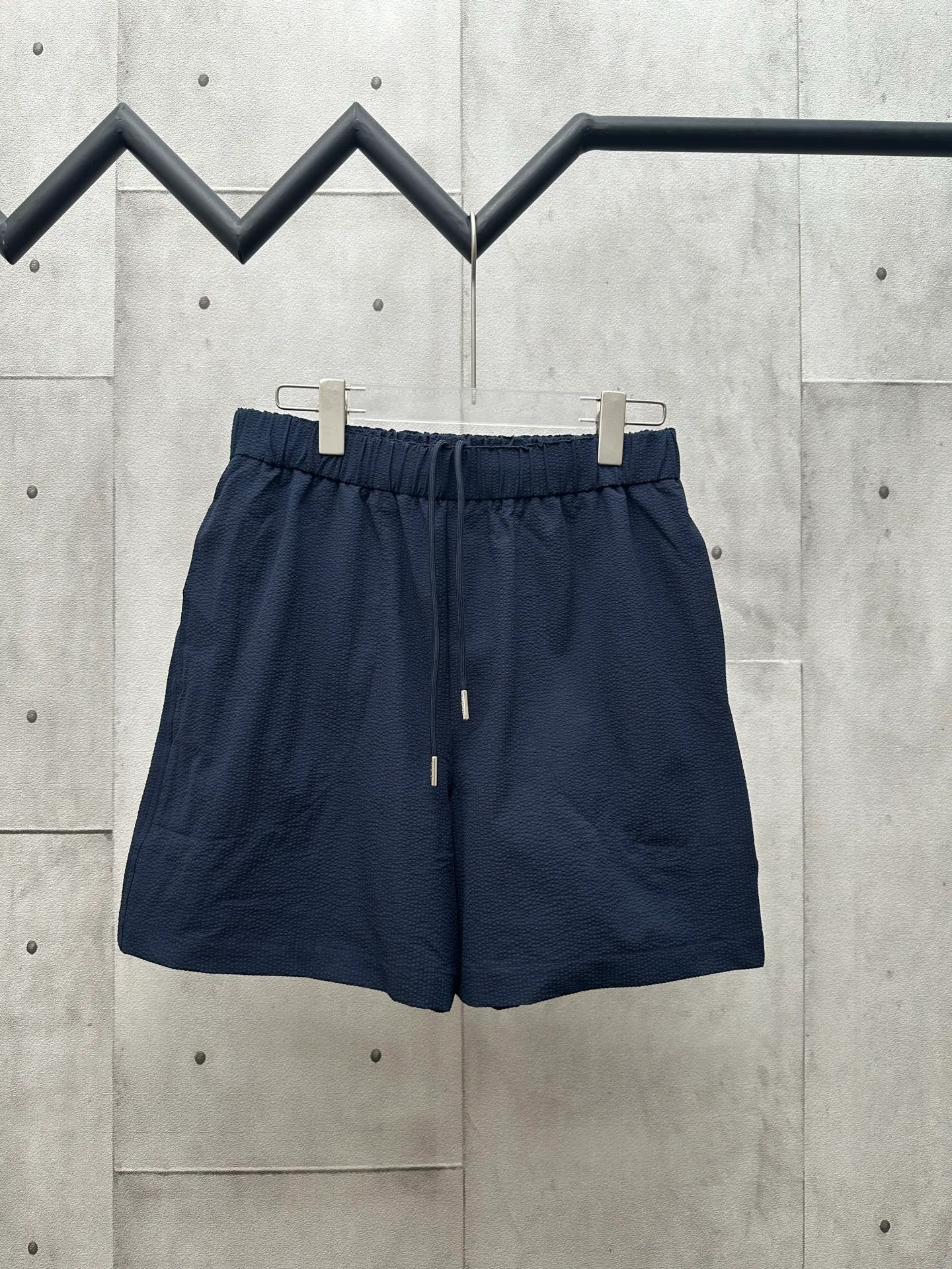 P320 MONCLER Puff Wrinkle Logo Shorts Fabric Selection: Made of cotton blended woven fabric with 76% high cotton content + 24% polyester fiber. The high cotton content ensures that the fabric is soft, skin-friendly, and has good breathability. The addition of a small amount of polyester fiber balances the wrinkle resistance and elasticity of the overall fabric and greatly reduces its shrinkage. After preshrinking, dimensional changes during washing are negligible. The fusion of the two makes the fabric combine anti-wrinkle, quick-drying, easy care and other characteristics without losing the advantages of good wearing experience and strong breathability.  Bubble wrinkle technology: ground warp + bubble warp independent let-off. The bubble warp yarn feeding speed is about 20% higher than the ground warp yarn feeding speed. During weaving, the bubble warp is relaxed and accumulated, forming a naturally arched bubble unit. Through the alternating arrangement of yarns + floating length tissue changes, a clear grid frame is built between the bubble units, and finally the bubble three-dimensional effect and grid outline are locked through high-temperature heat setting.  Accessories: One-to-one customized drawstring head One-to-one customized LOGO labeling SIZE: 1 2 3 4