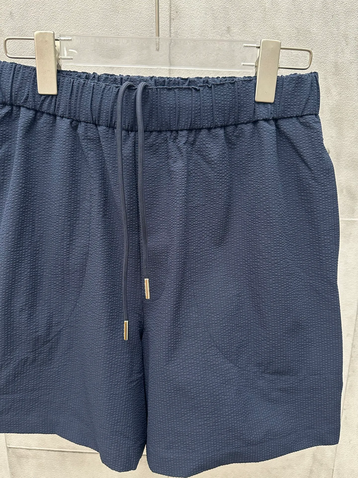 P320 MONCLER Puff Wrinkle Logo Shorts Fabric Selection: Made of cotton blended woven fabric with 76% high cotton content + 24% polyester fiber. The high cotton content ensures that the fabric is soft, skin-friendly, and has good breathability. The addition of a small amount of polyester fiber balances the wrinkle resistance and elasticity of the overall fabric and greatly reduces its shrinkage. After preshrinking, dimensional changes during washing are negligible. The fusion of the two makes the fabric combine anti-wrinkle, quick-drying, easy care and other characteristics without losing the advantages of good wearing experience and strong breathability.  Bubble wrinkle technology: ground warp + bubble warp independent let-off. The bubble warp yarn feeding speed is about 20% higher than the ground warp yarn feeding speed. During weaving, the bubble warp is relaxed and accumulated, forming a naturally arched bubble unit. Through the alternating arrangement of yarns + floating length tissue changes, a clear grid frame is built between the bubble units, and finally the bubble three-dimensional effect and grid outline are locked through high-temperature heat setting.  Accessories: One-to-one customized drawstring head One-to-one customized LOGO labeling SIZE: 1 2 3 4