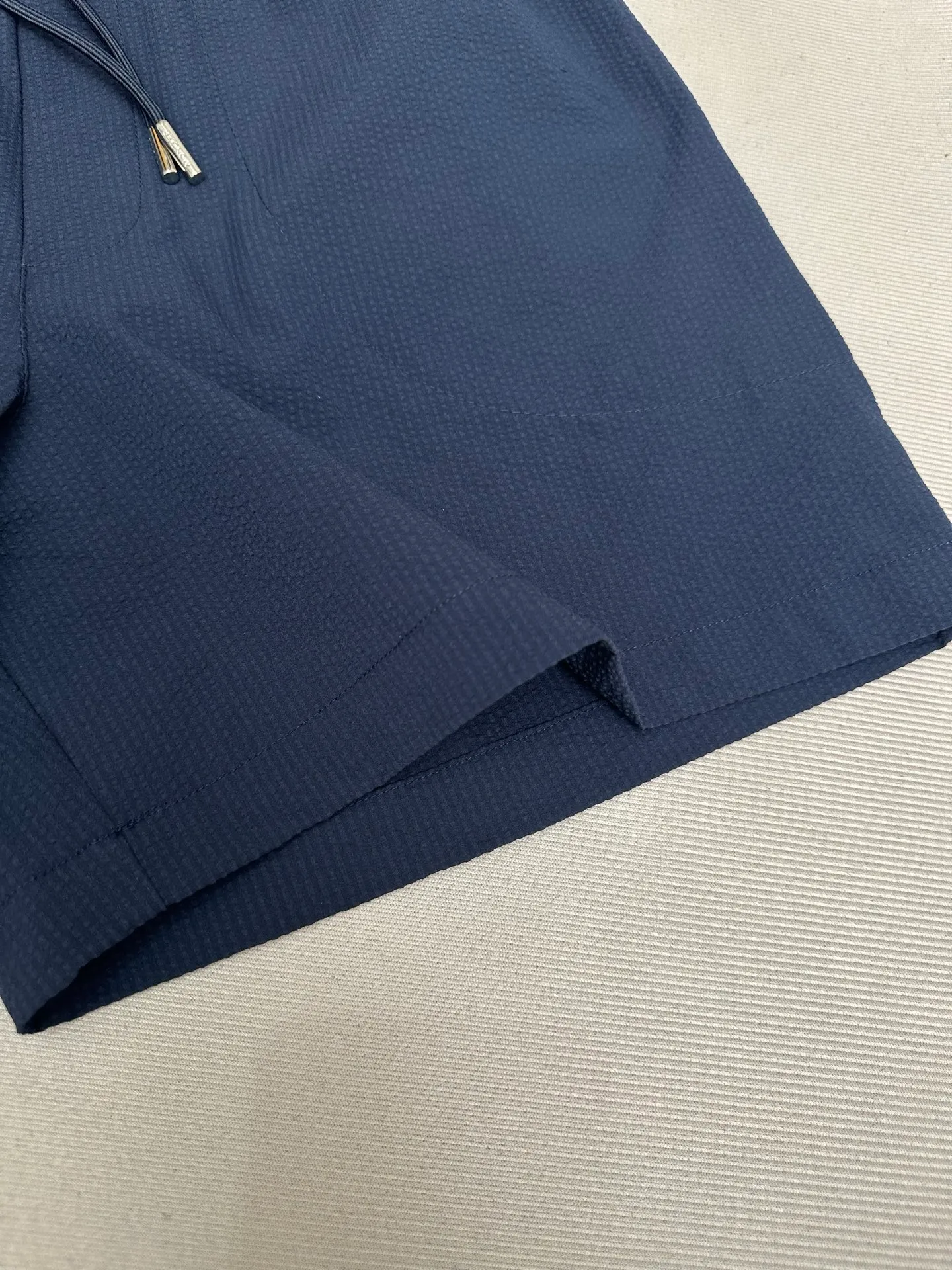 P320 MONCLER Puff Wrinkle Logo Shorts Fabric Selection: Made of cotton blended woven fabric with 76% high cotton content + 24% polyester fiber. The high cotton content ensures that the fabric is soft, skin-friendly, and has good breathability. The addition of a small amount of polyester fiber balances the wrinkle resistance and elasticity of the overall fabric and greatly reduces its shrinkage. After preshrinking, dimensional changes during washing are negligible. The fusion of the two makes the fabric combine anti-wrinkle, quick-drying, easy care and other characteristics without losing the advantages of good wearing experience and strong breathability.  Bubble wrinkle technology: ground warp + bubble warp independent let-off. The bubble warp yarn feeding speed is about 20% higher than the ground warp yarn feeding speed. During weaving, the bubble warp is relaxed and accumulated, forming a naturally arched bubble unit. Through the alternating arrangement of yarns + floating length tissue changes, a clear grid frame is built between the bubble units, and finally the bubble three-dimensional effect and grid outline are locked through high-temperature heat setting.  Accessories: One-to-one customized drawstring head One-to-one customized LOGO labeling SIZE: 1 2 3 4