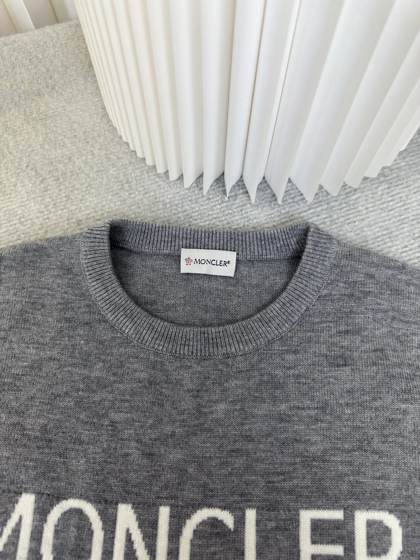 P440 MONCLER jacquard crew neck sweater is made of wool blended fabric, mainly 95% wool, combined with 4% nylon and 1% spandex. The main body of wool ensures the warmth and comfort of the clothing. The addition of a small amount of nylon and spandex significantly improves the elasticity and wear resistance. The ribbed decorative parts are made of 100% wool, which further enhances the overall texture.  Through the high needle count and fine gauge loom, combined with the orderly direction of the internal yarn, the floating threads are cleverly woven and stored, with almost no unnecessary thread mess. The color switching of each group of letters is synchronized with the knitting needles in milliseconds, forming a delicate letter LOGO jacquard decoration on the chest. Size S M L XL