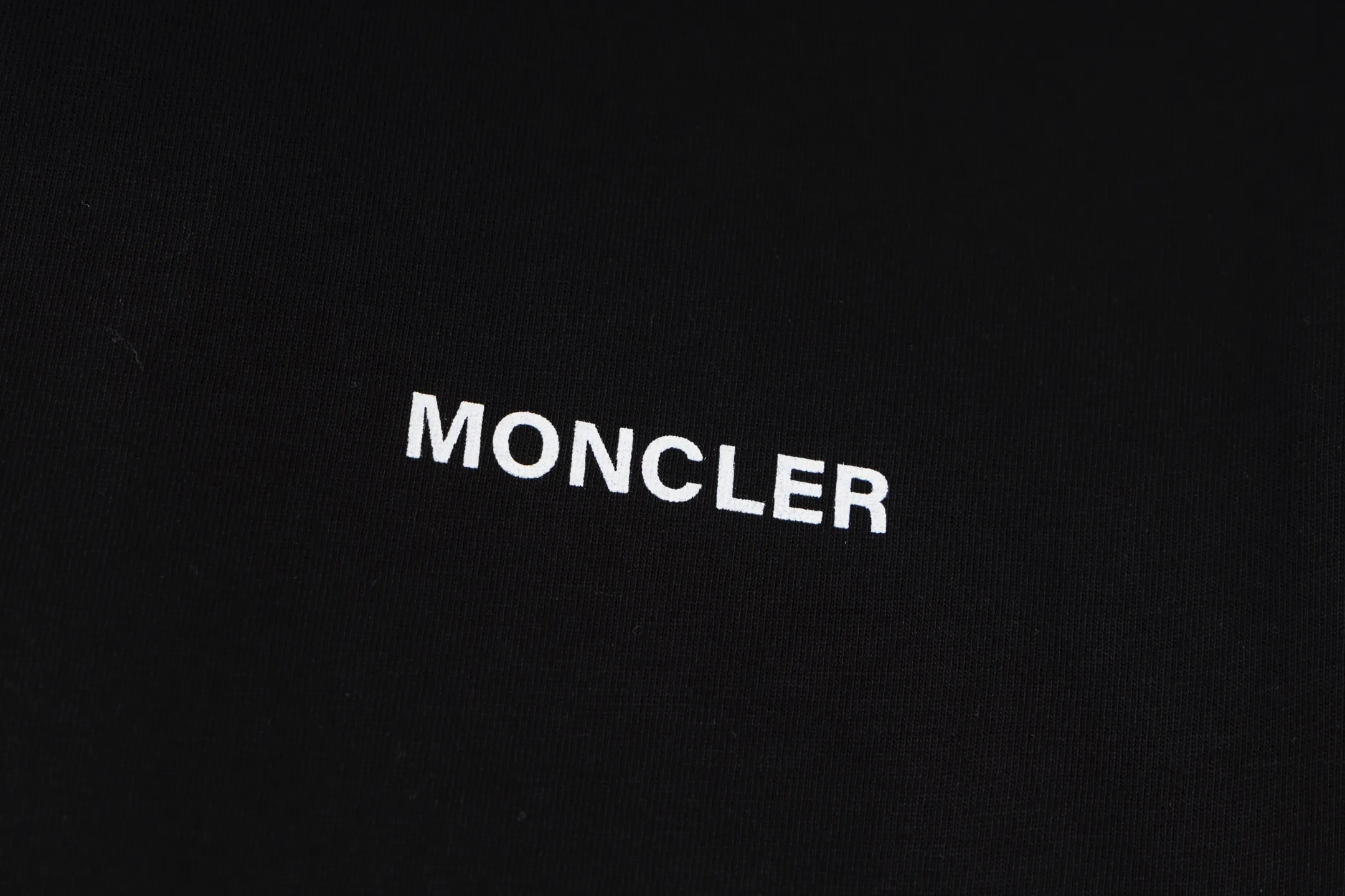 P230 exclusive supply] Moncler Hiroshi Fujiwara co-branded short-sleeve (black) is made of double-ply cotton plain fabric. The warp and weft yarns are interwoven one up and down to form a uniform grid-like texture, with a tight but light structure. Cotton fiber has natural breathability and skin-friendly properties. Combined with the pore structure of plain weave, it is suitable for daily perspiration needs and has good wearing comfort. The yarn has many intertwining points, which strengthens the tear resistance and can maintain its shape after multiple washings. Four high-saturation patterns are presented on the fabric through glue printing. The scraper pressure is even and the scraping is performed in three steps to ensure that the glue is fully penetrated and covered. After curing at high temperature, the pigment is firmly bonded to the cotton fiber. The ink-absorbing and penetrating properties of the cotton fiber make the pattern less likely to fall off due to friction. By actively interfering with the shrinkage potential of cotton fibers, the fabric is able to transition from changeable to stable, improving dimensional stability while being less prone to deformation and wrinkles. Size:S-M-L-XL