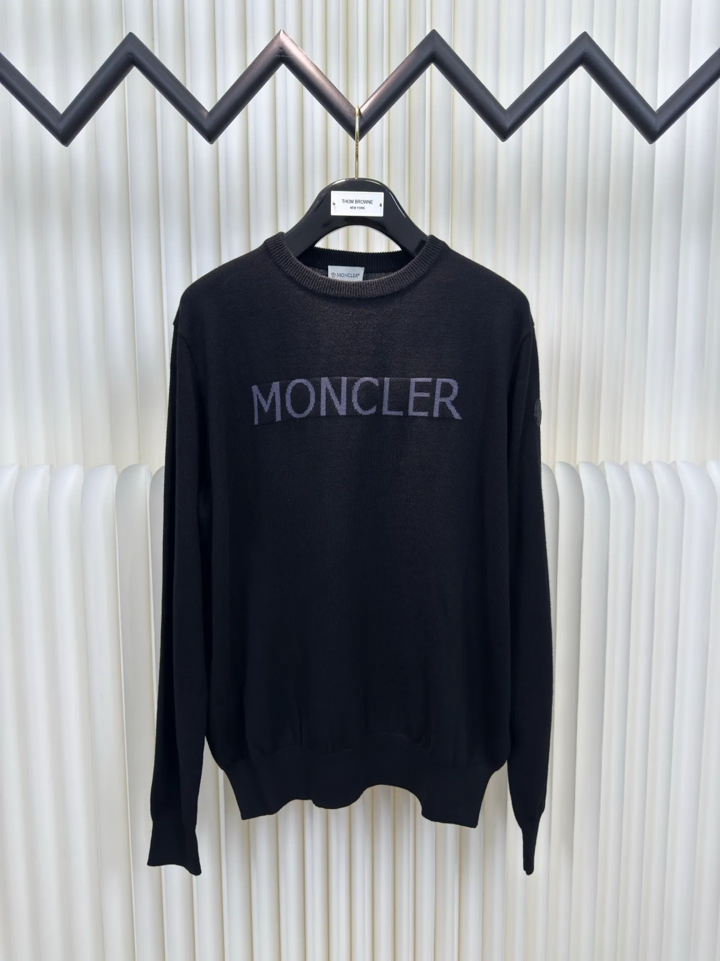 P440 MONCLER jacquard crew neck sweater is made of wool blended fabric, mainly 95% wool, combined with 4% nylon and 1% spandex. The main body of wool ensures the warmth and comfort of the clothing. The addition of a small amount of nylon and spandex significantly improves the elasticity and wear resistance. The ribbed decorative parts are made of 100% wool, which further enhances the overall texture.  Through the high needle count and fine gauge loom, combined with the orderly direction of the internal yarn, the floating threads are cleverly woven and stored, with almost no unnecessary thread mess. The color switching of each group of letters is synchronized with the knitting needles in milliseconds, forming a delicate letter LOGO jacquard decoration on the chest. Size S M L XL