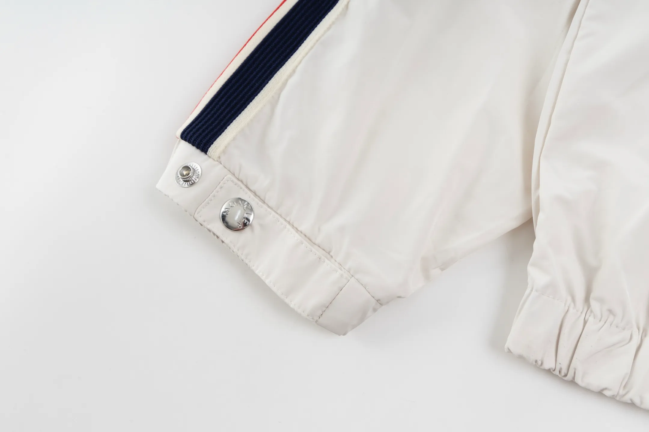 P550 Exclusive supply] Moncler Webbing Armband Lightweight Jacket (off-white) The fabric is made of 100% polyester fiber to create a tough protective outer layer. It is known for its excellent tear resistance and wear resistance. It can quickly return to flatness during wearing and maintain the crisp and stylish appearance of the clothing for a long time. At the same time, it is not easy to deform after being washed for a long time. Decorative edging in two different colors has been added to the center section of the sleeves. This design element not only adds visual highlights to the clothing, making it more fashionable and unique, the webbing is precisely positioned along the specified contours from the cuffs to the seam of the collar to ensure symmetry and overall smoothness. Before actual sewing, use very fine basting stitches for pre-fixing. This step is crucial to prevent the webbing from slipping, twisting, or wrinkling during sewing and ensuring that the final stitch is straight and perfect. Size:1/2/3/4