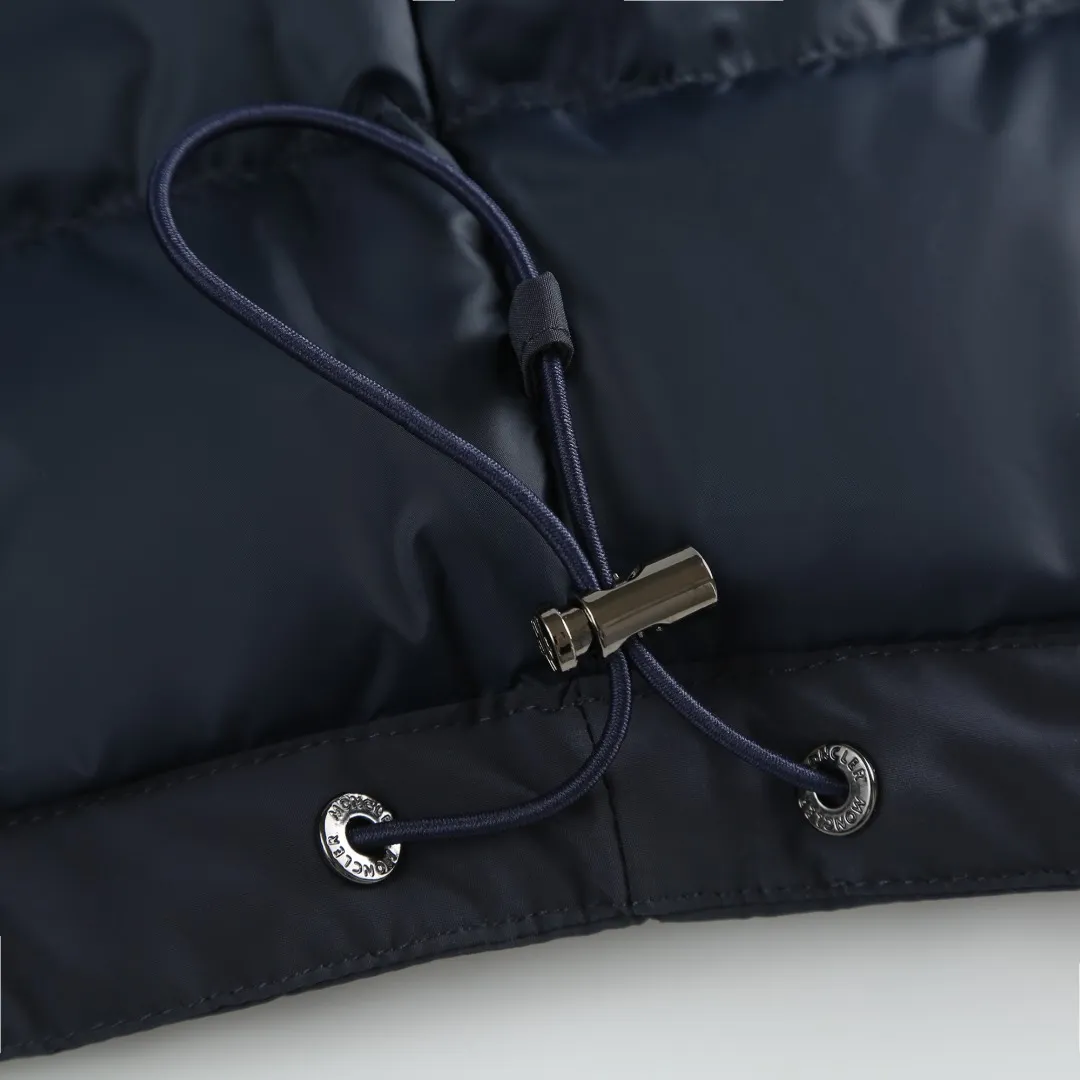 P860 MONCLER hooded jacket-style down jacket is made of 100% polyester fiber. After microfiberization treatment, the individual fibers become extremely fine, which greatly increases the fiber surface area, making the fabric soft and smooth, and the touch is close to natural fibers. The high-density textile method makes the structure tight, thus giving it a certain degree of wrinkle resistance, windproof warmth and wear resistance.  Lining selection: High-density lining fabric made of ultra-fine denier, 0.08mm thickness to avoid increasing the overall weight and making it smooth to wear. The high-density woven structure forms a wind resistance layer to protect the thermal efficiency of the thermal layer from loss. It can also withstand the expansion pressure of down and prevent deformation and damage after long-term use.  High-quality filling: 90 white duck down is selected, with a weight of 200g, ensuring excellent thermal insulation performance. After strict screening and treatment, the velvet is not easy to be drilled, ensuring durability. Details: The leather flap pocket on the chest is matched with a pebbled leather flap + matte metal buckle. It is low-key and exudes nobility. The hidden adjustment rope gives a sense of sophistication when you raise your hand. The "ID card" is directly embedded on the black satin inner patch pocket! Silver snaps + red, white and blue webbing, low-key yet exuding a sense of luxury, both visually and tactilely smooth.  Accessories: one-to-one customized buttons, one-to-one customized hem drawstring buckle, one-to-one customized phoenix eyes, one-to-one customized zipper pendant SIZE: 1 2 3 4