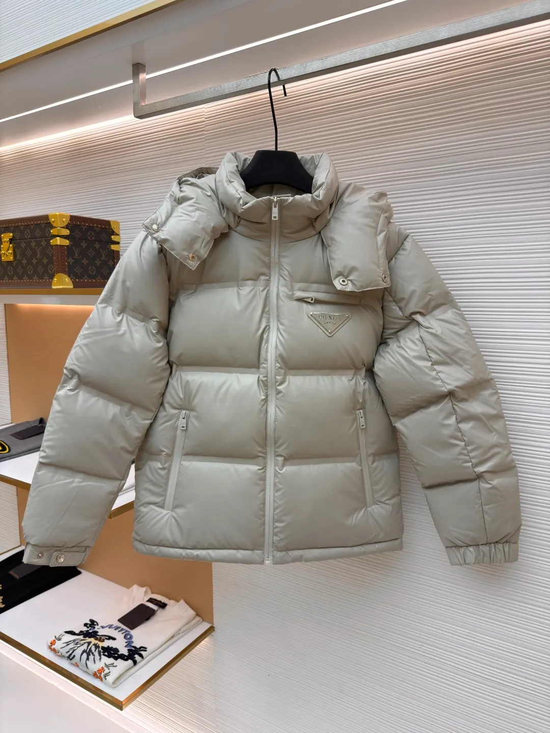 Prada solid color down jacket with removable hood ●Item number: 1682018-D15 ●Fabric: white duck down fabric ●Technology: mechanical down filling ●Color: light khaki gray ●Version: fitted version ●Weight: about 1070 grams ●Size: 48-50-52-54-56 ●Description: This Prada down jacket is made of regenerated nylon fabric, which is treated with high-density weaving and Teflon coating. It is waterproof and wrinkle-resistant and has a matte soft texture. The filling is made of 90% white duck down, and the down is locked in zones through 65-degree diagonal quilting technology. The stitch length is precisely controlled at 3 stitches/cm to avoid down fleece and give the body three-dimensional bulk. The detachable hood is fixed with metal snaps, and the bevel stitching on the neckline improves the fit; the triangle logo on the chest is presented in metal relief, seamlessly connecting with the same-color stitching on the body. The cuffs and hem are equipped with elastic ribs, the side invisible zipper pockets are hot-melt bonded, and the brand's customized hardware accessories are used in every detail, taking into account functionality and luxury texture. The overall wiring is straight and delicate, the fabric is comfortable and soft, and the color is consistent without color difference. It can be matched with the same style to create a fashionable look and control various occasions. Customized accessories, complete with three standards, same style for men and women!