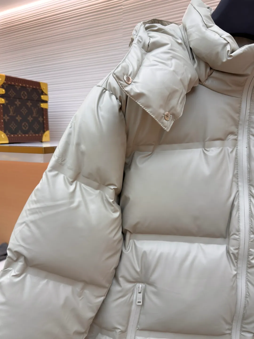 Prada solid color down jacket with removable hood ●Item number: 1682018-D15 ●Fabric: white duck down fabric ●Technology: mechanical down filling ●Color: light khaki gray ●Version: fitted version ●Weight: about 1070 grams ●Size: 48-50-52-54-56 ●Description: This Prada down jacket is made of regenerated nylon fabric, which is treated with high-density weaving and Teflon coating. It is waterproof and wrinkle-resistant and has a matte soft texture. The filling is made of 90% white duck down, and the down is locked in zones through 65-degree diagonal quilting technology. The stitch length is precisely controlled at 3 stitches/cm to avoid down fleece and give the body three-dimensional bulk. The detachable hood is fixed with metal snaps, and the bevel stitching on the neckline improves the fit; the triangle logo on the chest is presented in metal relief, seamlessly connecting with the same-color stitching on the body. The cuffs and hem are equipped with elastic ribs, the side invisible zipper pockets are hot-melt bonded, and the brand's customized hardware accessories are used in every detail, taking into account functionality and luxury texture. The overall wiring is straight and delicate, the fabric is comfortable and soft, and the color is consistent without color difference. It can be matched with the same style to create a fashionable look and control various occasions. Customized accessories, complete with three standards, same style for men and women!