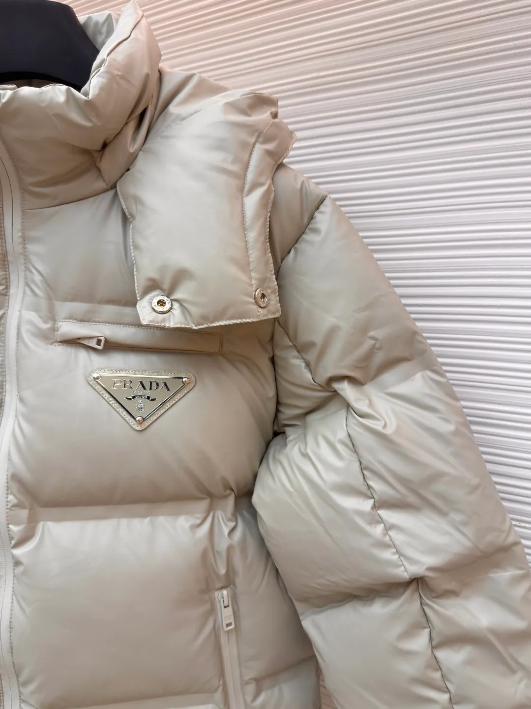 Prada solid color down jacket with removable hood ●Item number: 1682018-D15 ●Fabric: white duck down fabric ●Technology: mechanical down filling ●Color: light khaki gray ●Version: fitted version ●Weight: about 1070 grams ●Size: 48-50-52-54-56 ●Description: This Prada down jacket is made of regenerated nylon fabric, which is treated with high-density weaving and Teflon coating. It is waterproof and wrinkle-resistant and has a matte soft texture. The filling is made of 90% white duck down, and the down is locked in zones through 65-degree diagonal quilting technology. The stitch length is precisely controlled at 3 stitches/cm to avoid down fleece and give the body three-dimensional bulk. The detachable hood is fixed with metal snaps, and the bevel stitching on the neckline improves the fit; the triangle logo on the chest is presented in metal relief, seamlessly connecting with the same-color stitching on the body. The cuffs and hem are equipped with elastic ribs, the side invisible zipper pockets are hot-melt bonded, and the brand's customized hardware accessories are used in every detail, taking into account functionality and luxury texture. The overall wiring is straight and delicate, the fabric is comfortable and soft, and the color is consistent without color difference. It can be matched with the same style to create a fashionable look and control various occasions. Customized accessories, complete with three standards, same style for men and women!