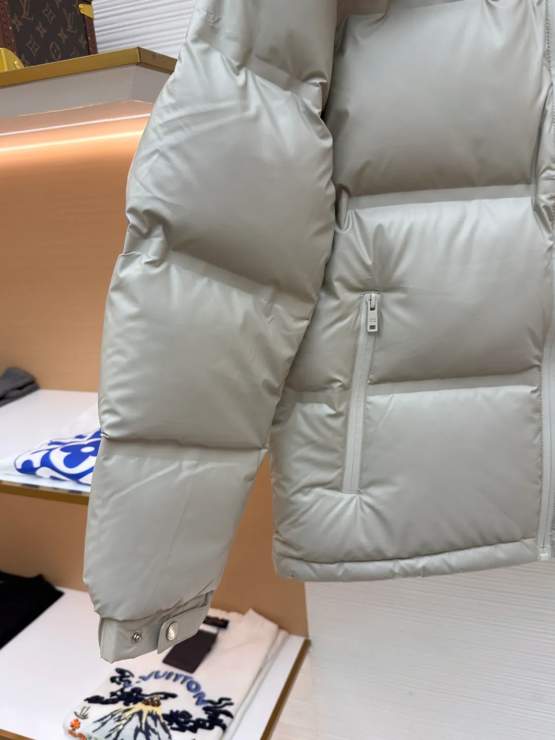Prada solid color down jacket with removable hood ●Item number: 1682018-D15 ●Fabric: white duck down fabric ●Technology: mechanical down filling ●Color: light khaki gray ●Version: fitted version ●Weight: about 1070 grams ●Size: 48-50-52-54-56 ●Description: This Prada down jacket is made of regenerated nylon fabric, which is treated with high-density weaving and Teflon coating. It is waterproof and wrinkle-resistant and has a matte soft texture. The filling is made of 90% white duck down, and the down is locked in zones through 65-degree diagonal quilting technology. The stitch length is precisely controlled at 3 stitches/cm to avoid down fleece and give the body three-dimensional bulk. The detachable hood is fixed with metal snaps, and the bevel stitching on the neckline improves the fit; the triangle logo on the chest is presented in metal relief, seamlessly connecting with the same-color stitching on the body. The cuffs and hem are equipped with elastic ribs, the side invisible zipper pockets are hot-melt bonded, and the brand's customized hardware accessories are used in every detail, taking into account functionality and luxury texture. The overall wiring is straight and delicate, the fabric is comfortable and soft, and the color is consistent without color difference. It can be matched with the same style to create a fashionable look and control various occasions. Customized accessories, complete with three standards, same style for men and women!