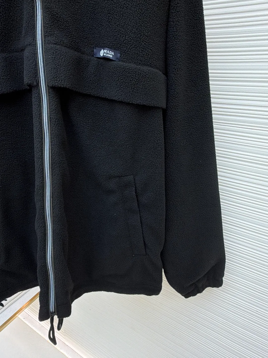 Prada Polar Fleece Jacket ●Original version: Purchased and developed by 13138 ●Item No.: 1682329-B50 ●Fabric: Polar fleece fabric ●Technology: Positioned cutting machine production ●Color: black ●Version: Fitted version ●Weight: about 635 grams ●Size: S-M-L-XL ●Description: The woven fabric is brushed, that is, the fiber surface is fluffed through mechanical brushing to form fluff. Then the shaking process is carried out. The fabric is shaken under high temperature and humid conditions, so that the fibers form small spherical particles, which increases the fluffiness and warmth of the fabric. Polar fleece fabric undergoes a dyeing process to ensure uniform and long-lasting color. After dyeing, the fabric undergoes finishing processes such as shaping and calendering to improve the feel and appearance. Splice the cut parts (such as front and back panels, sleeves, hats, etc.) according to the design requirements. When splicing, you need to pay attention to aligning the seams to ensure that the splicing is smooth and wrinkle-free. For parts that are prone to wear, such as collars, cuffs, and hems, hemming is used to increase elasticity and durability. At the same time, details such as zippers and pockets also need to be carefully processed to ensure functionality and aesthetics. Choose high-quality metal zippers to ensure that the zippers are smooth and durable. The color of the zipper needs to be coordinated with the color of the main body of the jacket to enhance the overall aesthetics. The overall wiring is straight. Delicate, the fabric is comfortable and soft, the color is consistent and there is no color difference. It can be matched with the same style to create a fashionable look and control various occasions. Customized accessories, complete with three standards, same style for men and women!