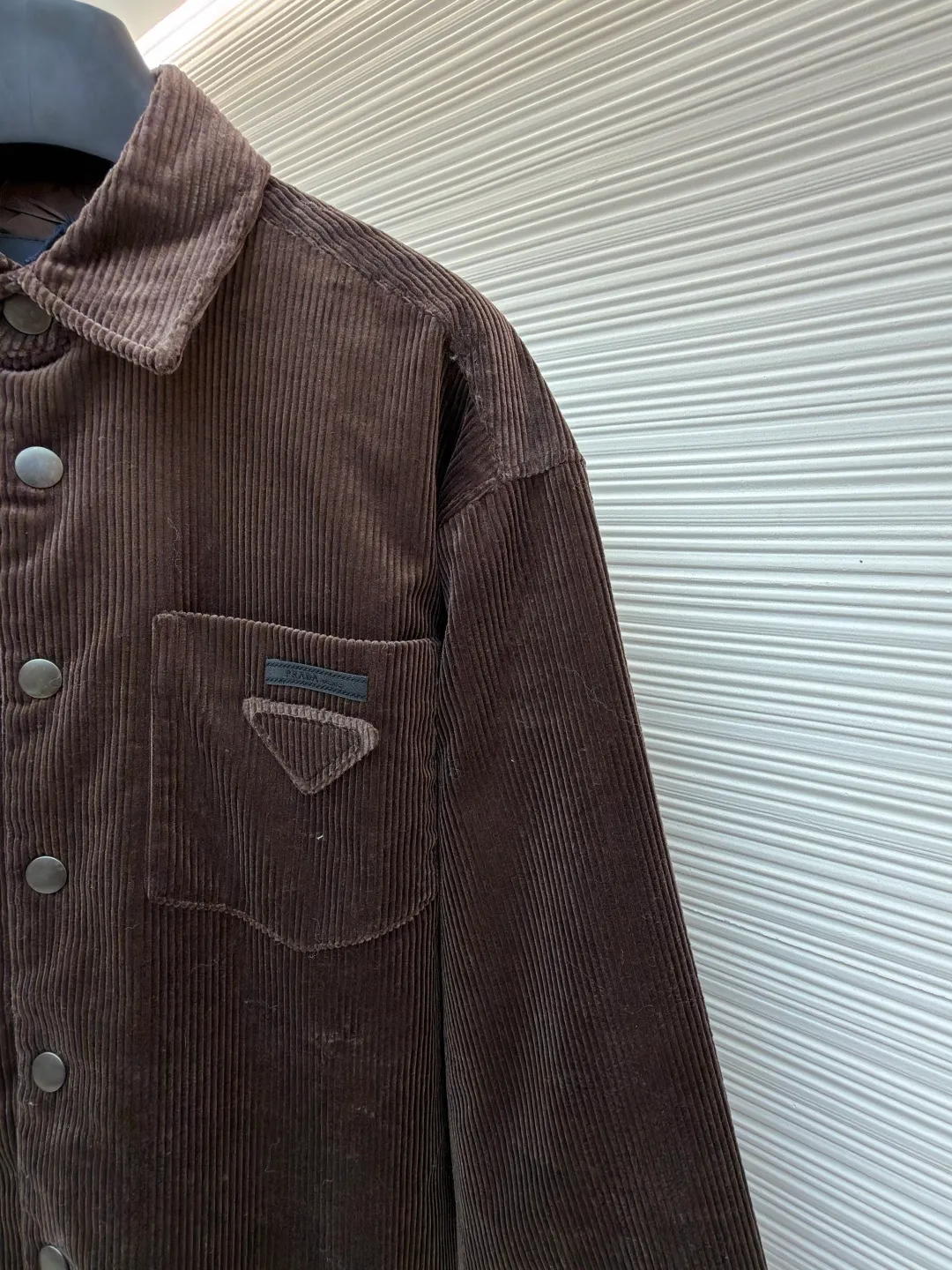 Prada triangle logo corduroy cotton jacket ●Original version: purchased and developed by 10012 ●Item number: 1682236-B90 ●Fabric: corduroy fabric ●Technology: made on positioning cutting machine ●Color: brown ●Version: fitted version ●Weight: about 745 grams ●Size: XS-S-M-L ●Description: This brown corduroy shirt-style jacket is made of high-count combed cotton corduroy fabric. It has been treated with pre-washing water. The fabric velvet is even in thickness, soft and waxy to the touch, and not easy to pill and deform. It also has good drape and wrinkle resistance. The body is cut into a loose shirt silhouette, and the shoulders are designed with natural dropped shoulders. Combined with three-dimensional tailoring technology, the shape is more ergonomic. The placket is made of matte metal snaps, treated with anti-oxidation plating, which makes it high-quality and durable. The triangular patch pocket on the chest is equipped with the brand's metal logo plate, which is fixed with manual caulking and has neat edges. The collar and cuffs are double-layered and reinforced, the sewing stitches are fine and even, and the spacing of each inch of stitches is strictly controlled. The overall workmanship combines practicality and exquisiteness, fully demonstrating the craftsmanship. The overall wiring is straight and delicate, the fabric is comfortable and soft, and the color is consistent without color difference. It can be matched with the same style to create a fashionable look and control various occasions. Customized accessories, complete with three standards, same style for men and women!