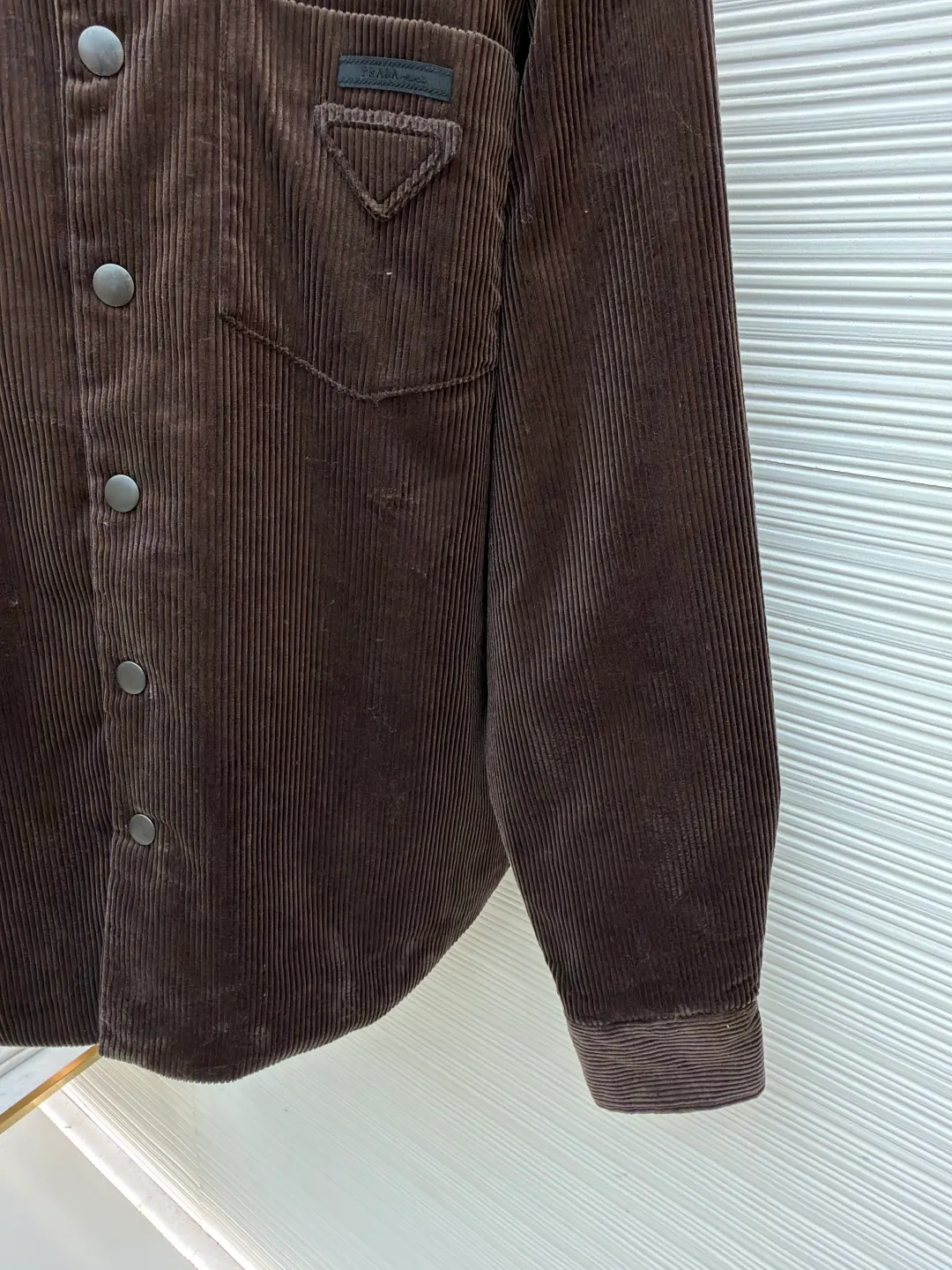 Prada triangle logo corduroy cotton jacket ●Original version: purchased and developed by 10012 ●Item number: 1682236-B90 ●Fabric: corduroy fabric ●Technology: made on positioning cutting machine ●Color: brown ●Version: fitted version ●Weight: about 745 grams ●Size: XS-S-M-L ●Description: This brown corduroy shirt-style jacket is made of high-count combed cotton corduroy fabric. It has been treated with pre-washing water. The fabric velvet is even in thickness, soft and waxy to the touch, and not easy to pill and deform. It also has good drape and wrinkle resistance. The body is cut into a loose shirt silhouette, and the shoulders are designed with natural dropped shoulders. Combined with three-dimensional tailoring technology, the shape is more ergonomic. The placket is made of matte metal snaps, treated with anti-oxidation plating, which makes it high-quality and durable. The triangular patch pocket on the chest is equipped with the brand's metal logo plate, which is fixed with manual caulking and has neat edges. The collar and cuffs are double-layered and reinforced, the sewing stitches are fine and even, and the spacing of each inch of stitches is strictly controlled. The overall workmanship combines practicality and exquisiteness, fully demonstrating the craftsmanship. The overall wiring is straight and delicate, the fabric is comfortable and soft, and the color is consistent without color difference. It can be matched with the same style to create a fashionable look and control various occasions. Customized accessories, complete with three standards, same style for men and women!