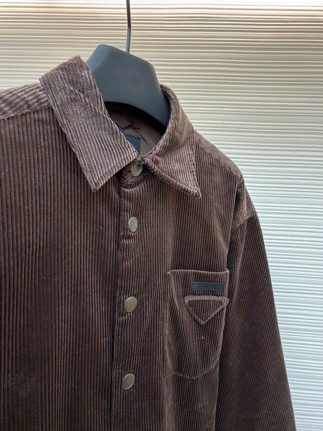 Prada triangle logo corduroy cotton jacket ●Original version: purchased and developed by 10012 ●Item number: 1682236-B90 ●Fabric: corduroy fabric ●Technology: made on positioning cutting machine ●Color: brown ●Version: fitted version ●Weight: about 745 grams ●Size: XS-S-M-L ●Description: This brown corduroy shirt-style jacket is made of high-count combed cotton corduroy fabric. It has been treated with pre-washing water. The fabric velvet is even in thickness, soft and waxy to the touch, and not easy to pill and deform. It also has good drape and wrinkle resistance. The body is cut into a loose shirt silhouette, and the shoulders are designed with natural dropped shoulders. Combined with three-dimensional tailoring technology, the shape is more ergonomic. The placket is made of matte metal snaps, treated with anti-oxidation plating, which makes it high-quality and durable. The triangular patch pocket on the chest is equipped with the brand's metal logo plate, which is fixed with manual caulking and has neat edges. The collar and cuffs are double-layered and reinforced, the sewing stitches are fine and even, and the spacing of each inch of stitches is strictly controlled. The overall workmanship combines practicality and exquisiteness, fully demonstrating the craftsmanship. The overall wiring is straight and delicate, the fabric is comfortable and soft, and the color is consistent without color difference. It can be matched with the same style to create a fashionable look and control various occasions. Customized accessories, complete with three standards, same style for men and women!
