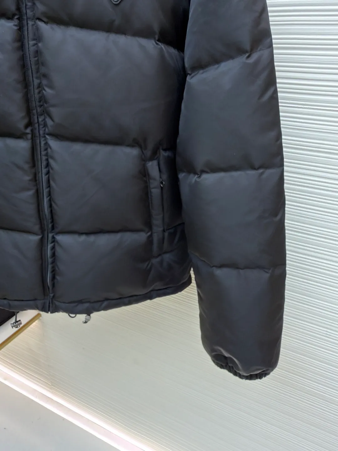 Prada nylon triangle down jacket ●Original version: Purchased and developed by 13557 ●Item number: 1681282-C95 ●Fabric: white duck down fabric ●Technology: mechanical down filling ●Color: black ●Version: fitted version ●Weight: about 1025 grams ●Size: S-M-L-XL ●Description: Made of high-count and high-density nylon woven fabric, it is a lightweight, strong and fine-textured advanced fabric. Its physical complexity lies in the fact that while achieving extreme lightweight, it provides excellent tear resistance and abrasion resistance through a dense fabric structure, solving the industry problem of light weight and durability that are often contradictory. Waterproof coating: This is not a simple film, but a microscopic functional polymer layer coated on the surface of the fabric after it is woven. Its complexity is reflected in its chemical properties: it can effectively reduce the surface tension of the fabric, making it impossible for water droplets to penetrate its fiber gaps, thereby forming a lotus leaf effect and achieving efficient waterproofing. At the same time, this coating usually has a certain degree of breathability, allowing moisture emitted by the body to escape and maintaining a comfortable internal microclimate. This is a precise balancing technology. The laser-burned triangle mark on the chest is the pinnacle of the complexity of the entire garment's craftsmanship. Laser burning is a non-contact precision processing technology. Using a laser beam of specific wavelength and energy, the fibers on the surface of the fabric are vaporized according to a preset digital path. The laser can accurately "carve" every detail of the logo without damaging the underlying fabric structure, with clear and sharp edges and a unique, slightly burning matte texture. This is completely different from traditional embroidery or offset printing. It is integrated with the fabric itself and cannot be peeled off. It also requires extremely high stability in process control - if the energy is slightly weaker, the pattern will be unclear, and if the energy is slightly stronger, it may penetrate the fabric. The core is filled with 90% pure white duck down. "90% pure white duck down" is an indicator that has been strictly sorted. The thermal insulation principle of down is that its three-dimensional velvet can hold a large amount of still air and form an efficient thermal insulation layer. To sum up, every part of this down jacket goes beyond basic functions and embodies full-link innovation and quality control from raw material selection, textile engineering, chemical processing to digital finishing. The overall wiring is straight and delicate, the fabric is comfortable and soft, and the color is consistent without color difference. It can be matched with the same style to create a fashionable look and control various occasions. Customized accessories, complete with three standards, same style for men and women!