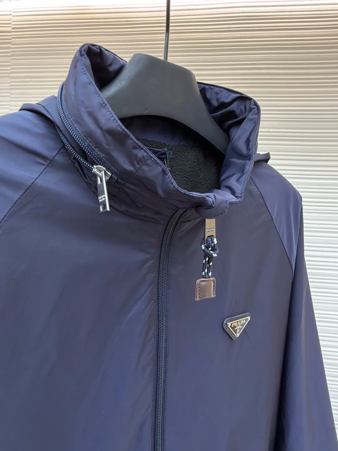 Prada Regenerated Nylon Fleece Jacket ●Original version: Purchased and developed by 12048 ●Item number: 1682331-B70 ●Fabric: Regenerated nylon fabric ●Technology: Made on positioning cutting machine ●Color: Navy blue ●Version: Fitted version ●Weight: about 585 grams ●Size: S-M-L-XL ●Description: High-density yarn is made by melt spinning through a special process. The yarn has been stretched and twisted through multiple processes to give the fabric the stiffness and wrinkle resistance that are comparable to those of native materials, while retaining a light and drapey wearing experience. The surface of the fabric is treated with an environmentally friendly coating process to form a micro-waterproof film layer, which is both windproof and breathable. The main raw material is polyester fiber blended wool raw material which is cleaned and pre-treated to remove impurities. After the yarn is woven into fabric through a loom, it is brushed, that is, the surface of the fiber is fluffed through mechanical brushing to form fluff. Then the shaking process is carried out, and the fabric is shaken under high temperature and humid conditions, so that the fibers form small spherical particles to increase the thermal insulation performance. The shoulder splicing uses twill sewing technology, the raglan sleeve design releases shoulder movement space, and the regular shoulder line ensures the stiffness of the overall silhouette, maintaining an elegant silhouette for both sports and static wear. The three-dimensional pleat design is incorporated into both sides of the body and sleeve elbows, and a long-lasting pleat texture is formed through high-temperature setting technology. This not only enhances the aerodynamic performance of the fabric, but also enriches the visual hierarchy with light and shadow changes, breaking the dull feeling of solid color fabrics. The cuffs are equipped with a hidden snap-button adjustment system, which can be freely tightened according to the circumference of the wrist to prevent cold wind from entering; the straight bottom edge is matched with a drawstring at the hem, and the inner rope buckle design can be used to adjust the tightness, taking into account warmth preservation and waistline shaping. The overall wiring is straight and delicate, the fabric is comfortable and soft, and the color is consistent without color difference. It can be matched with the same style to create a fashionable look and control various occasions. Customized accessories, complete with three standards, same style for men and women!