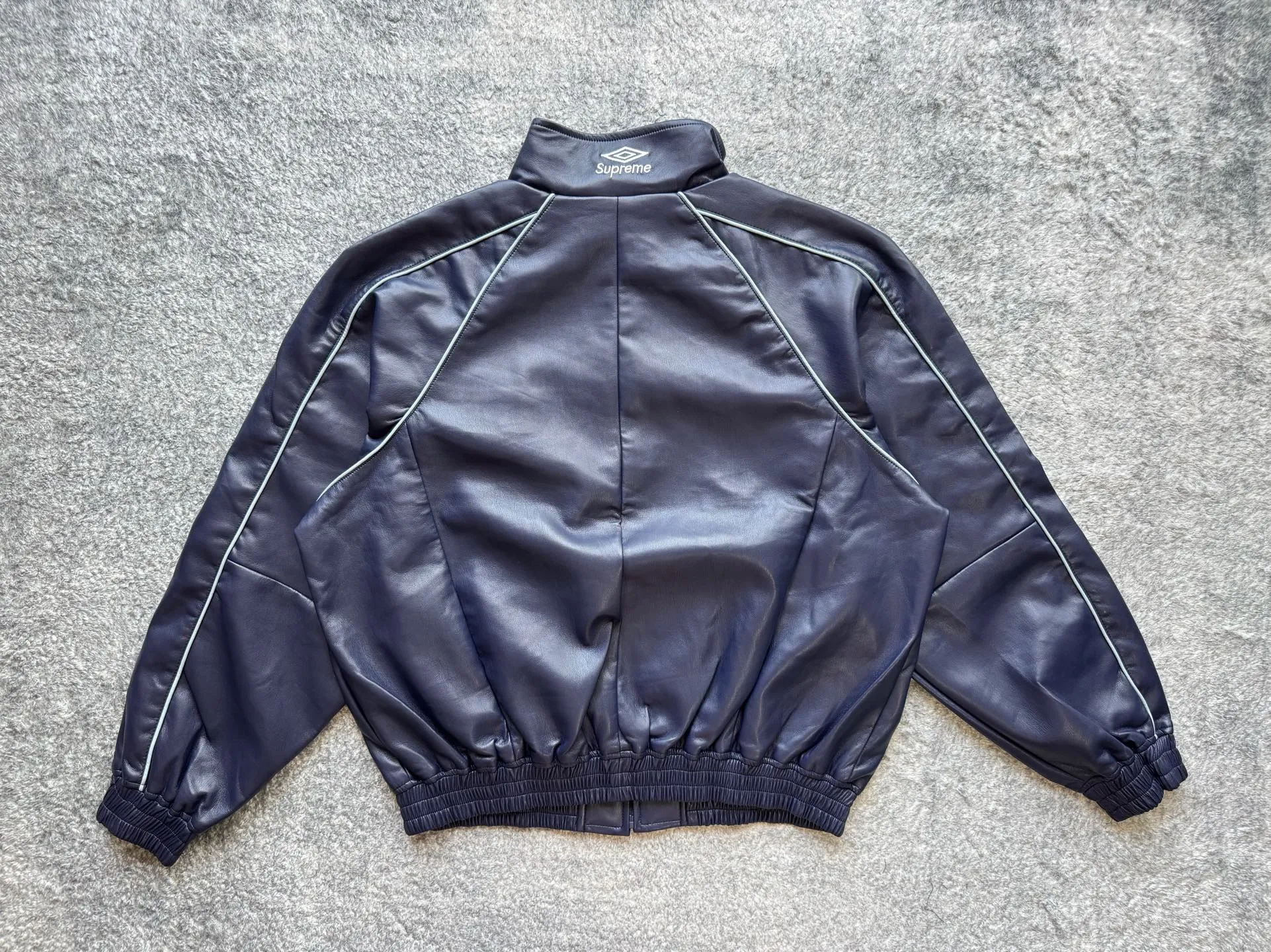 P590 Supreme Umbro joint model FW25 WEEK4 Leather Track Jacket embroidered logo zipper closure leather jacket, same style for men and women, made of lambskin material, mesh lining. Welted zippered hand pockets at lower front and internal chest pocket. Elasticized cuffs and hem in leather. Embroidered logo at chest and back neck. Color: Black, Navy, Pink Size: S M L